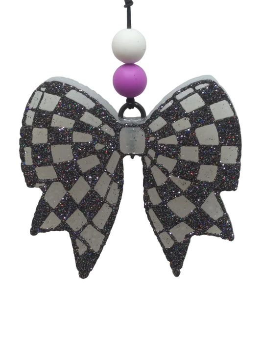 Decorative Bow shaped car air freshener with checkered pattern in black glitter on a white base. purple and whte beads decorate the elastic hanger. 