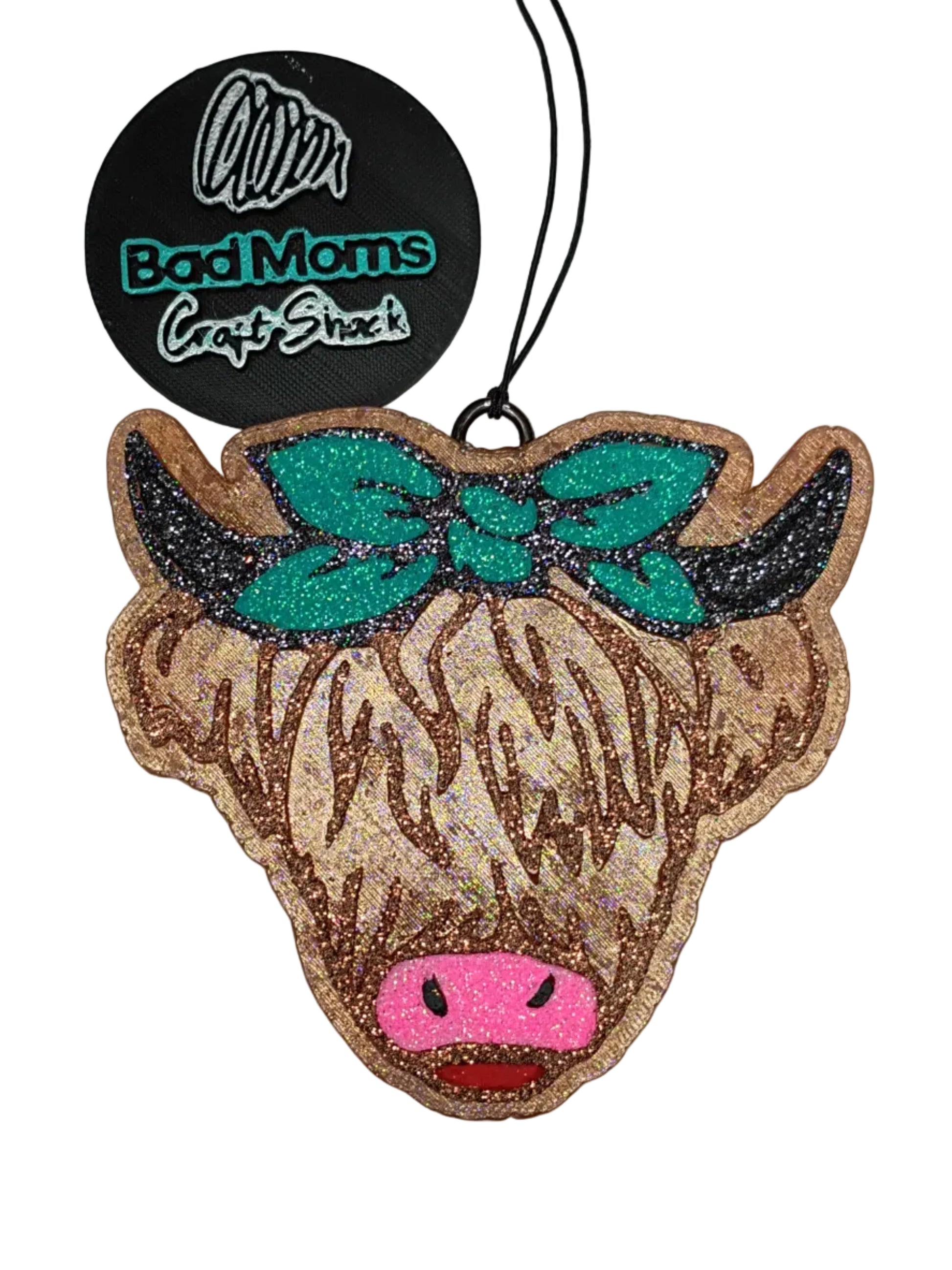 Highland cow shaped car freshener-with raised details. Rose gold glitter hair with black glitter horns, a pink glitter nose, red glitter tongue and a handkercheif style bow in teal glitter outlined in black glitter on a broze brown base. 