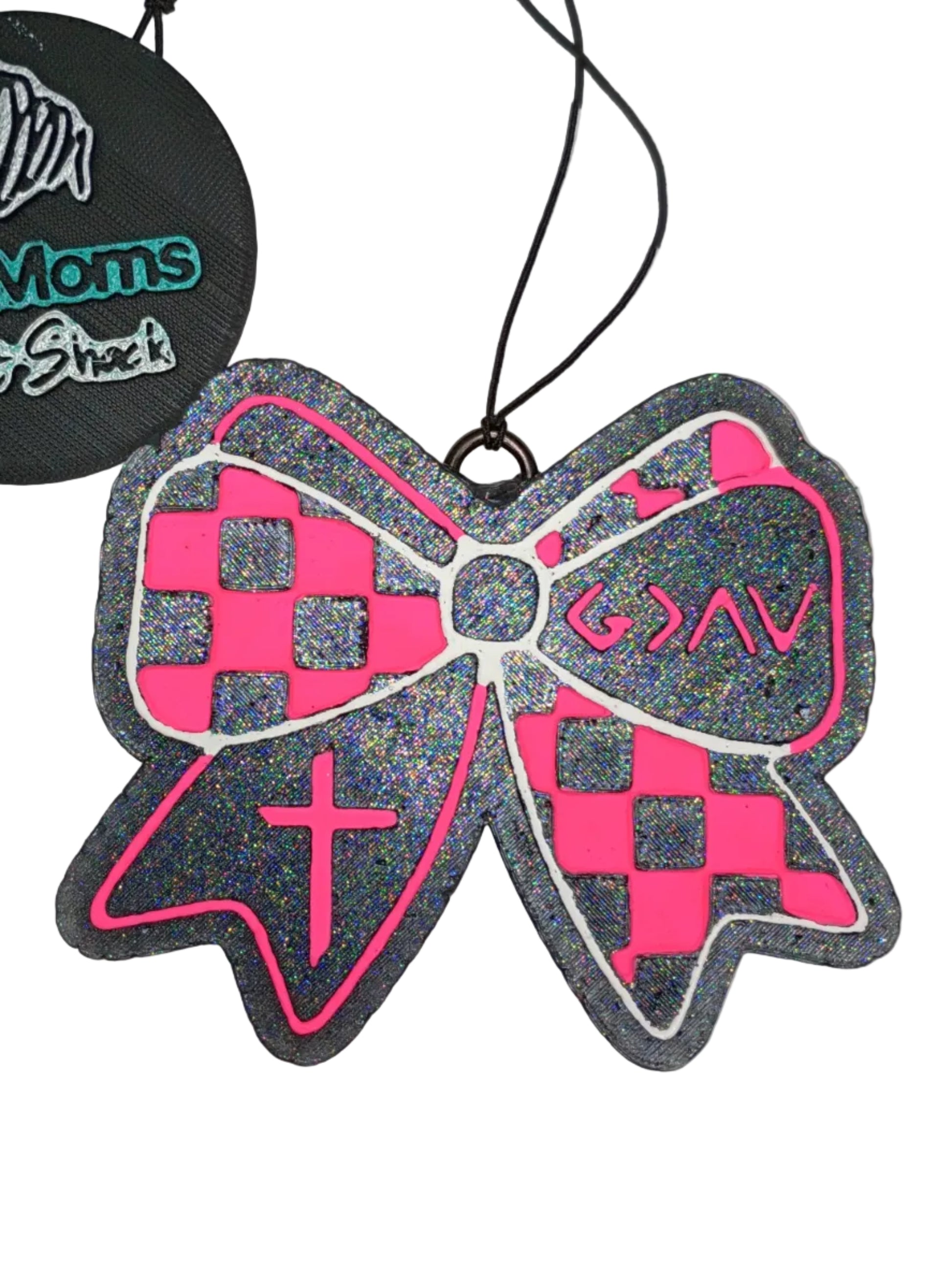 Hot pink and white checkered bow-shaped car freshener on a black base.  The symbols are painted in hot pink on opposite sides of the checkerboard design. It has a pink and white detailed outline around the bow.