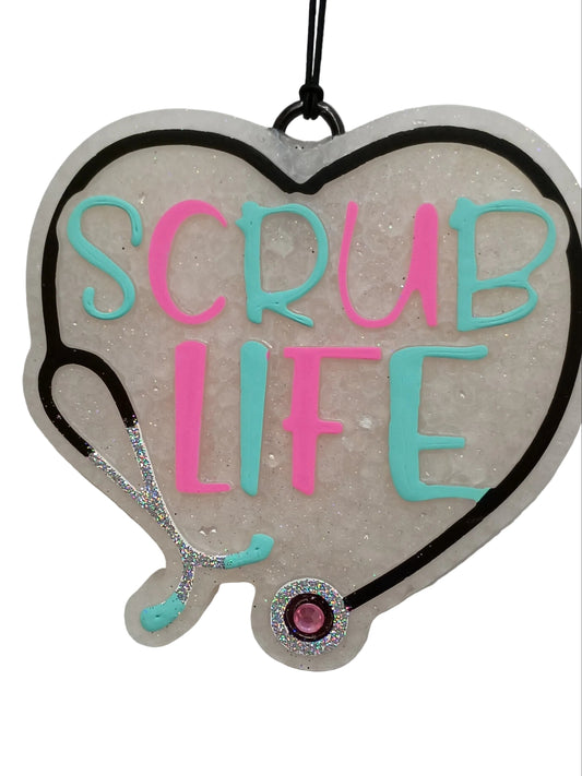 Heart-shaped freshener with 'SCRUB LIFE' text in pink and teal paint . A black stethoscope design outline with silver glitter details and a pink rhinestone accent on a white base.