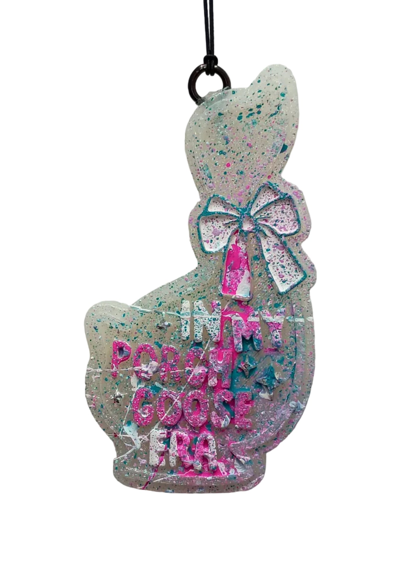 Goose shaped hanging air freshener  with lettering that says 'In my porch goose era" decorated in a pink, teal and white splatter paint theme on a white base. 