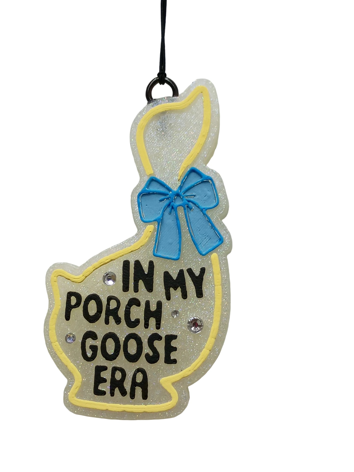 Decorative goose shaped car freshener  with 'In My Porch Goose Era' text  in black , a blue bow and yellow outline around the goose on a white base. 3 rhinestones scattered around the lettering.